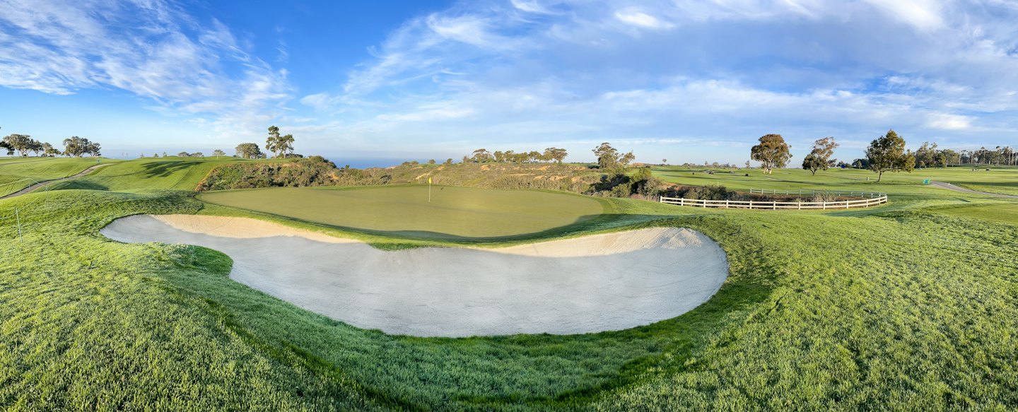 A sand bunker sits beside a manicured green on a golf course.